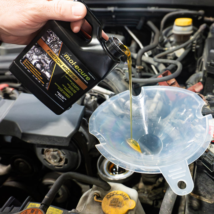 A hand pours a container of Molecure™ Catalytic Restore Emission Treatment into a clear funnel above a car engine.